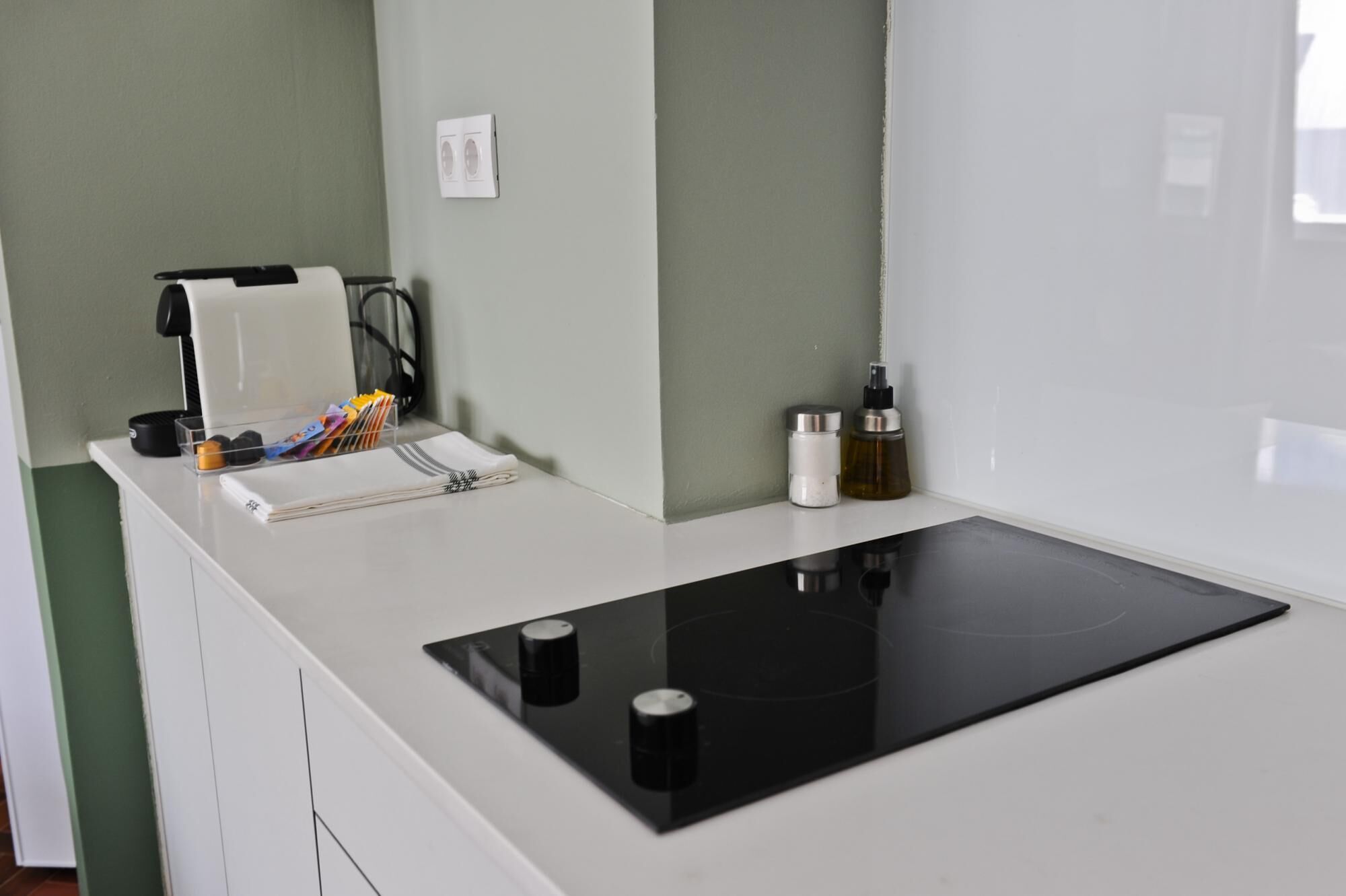 A kitchen with a black induction cooktop, a coffee maker, and a small shelf with kitchen essentials.