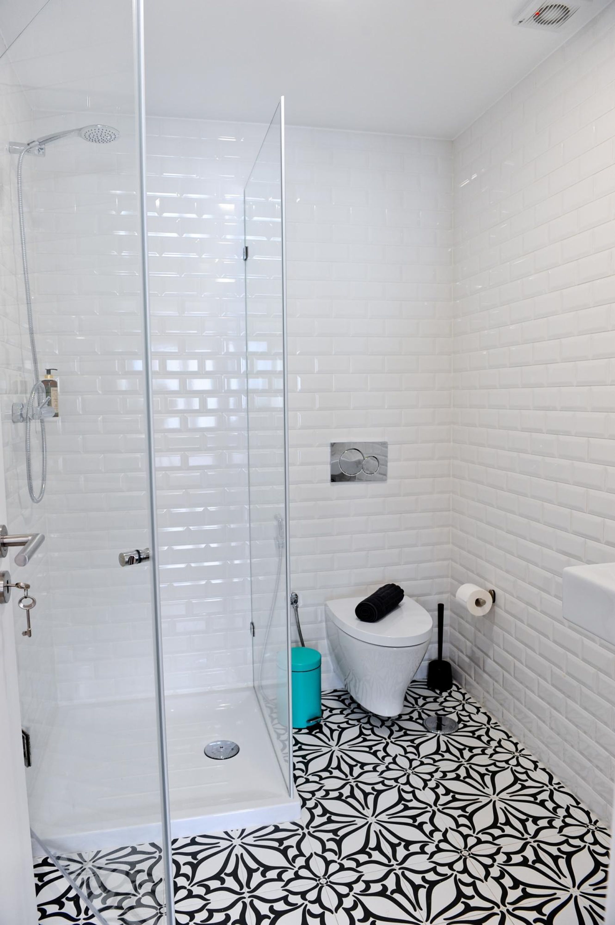 A bathroom with a glass shower enclosure, white tiled walls, a toilet, and a patterned floor.