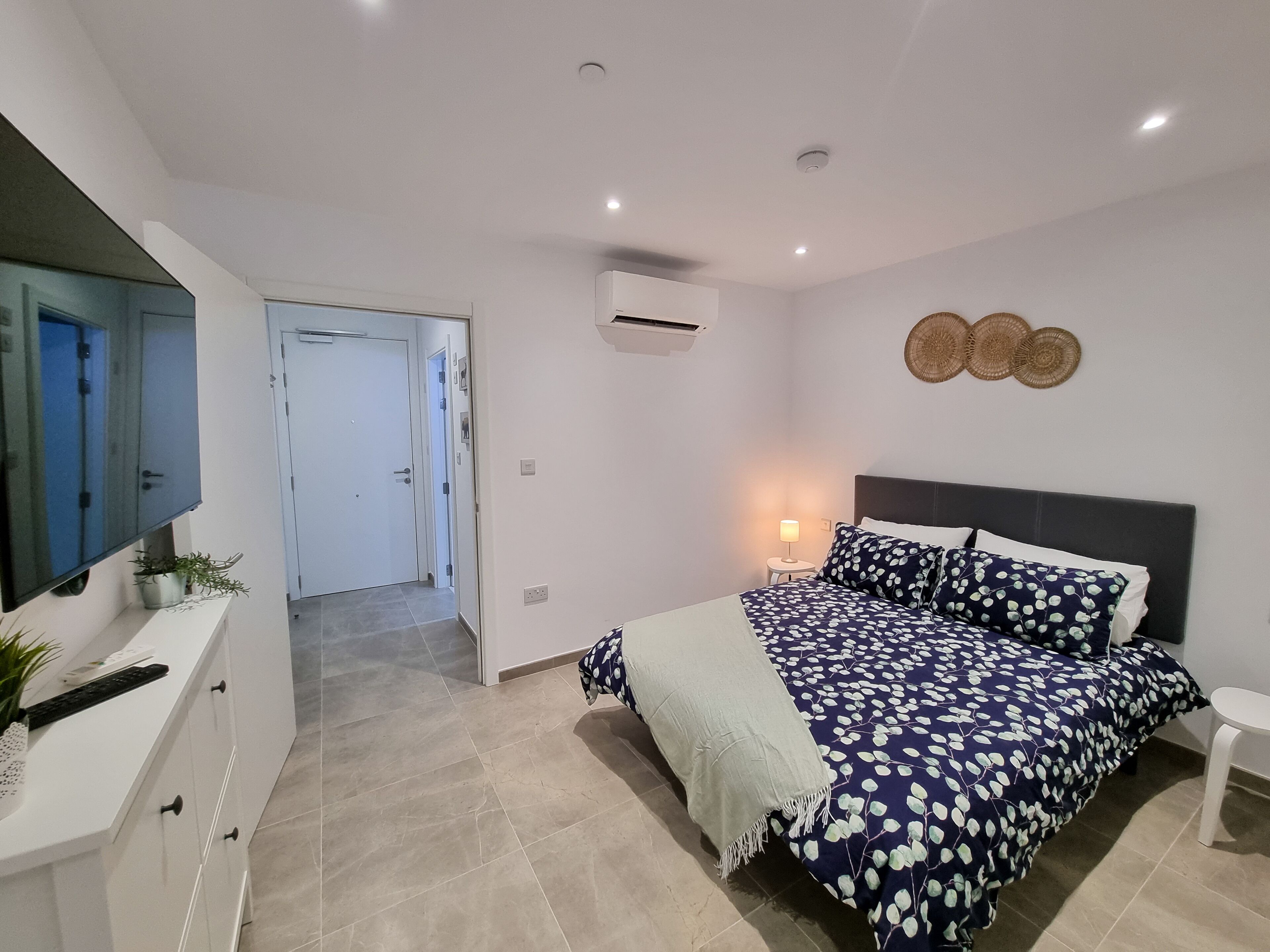 Un dormitorio con cama, mesita de noche y televisor montado en la pared.