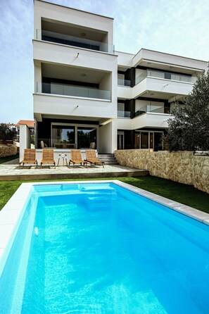 Un moderno edificio de dos pisos con piscina, mobiliario exterior y un muro de piedra.