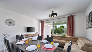 Un salon moderne comprenant un coin repas, un téléviseur à écran plat et une grande fenêtre avec des rideaux.