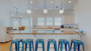 A modern kitchen with a large island, bar stools, and a dining area with a chandelier. - Biscayne Seaglass: 4 BR, 3 BA House in Port Bolivar, Sleeps 12 (Bolivar Peninsula)