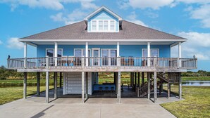 A two-story house with a balcony, a covered porch, and a view of a lake. - Biscayne Seaglass: 4 BR, 3 BA House in Port Bolivar, Sleeps 12 (Bolivar Peninsula)