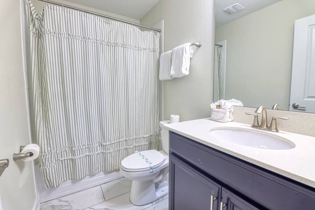 A bathroom with a striped shower curtain, a toilet, a sink with a mirror, and a towel rack.