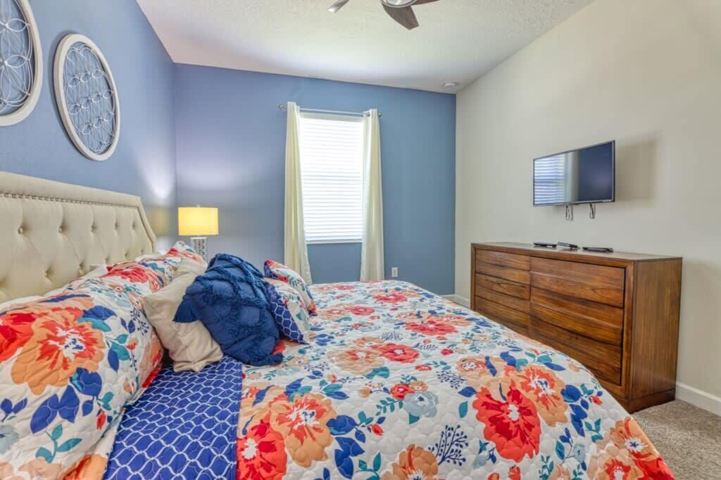 A bedroom with a bed, a dresser, a television, and a window with curtains.