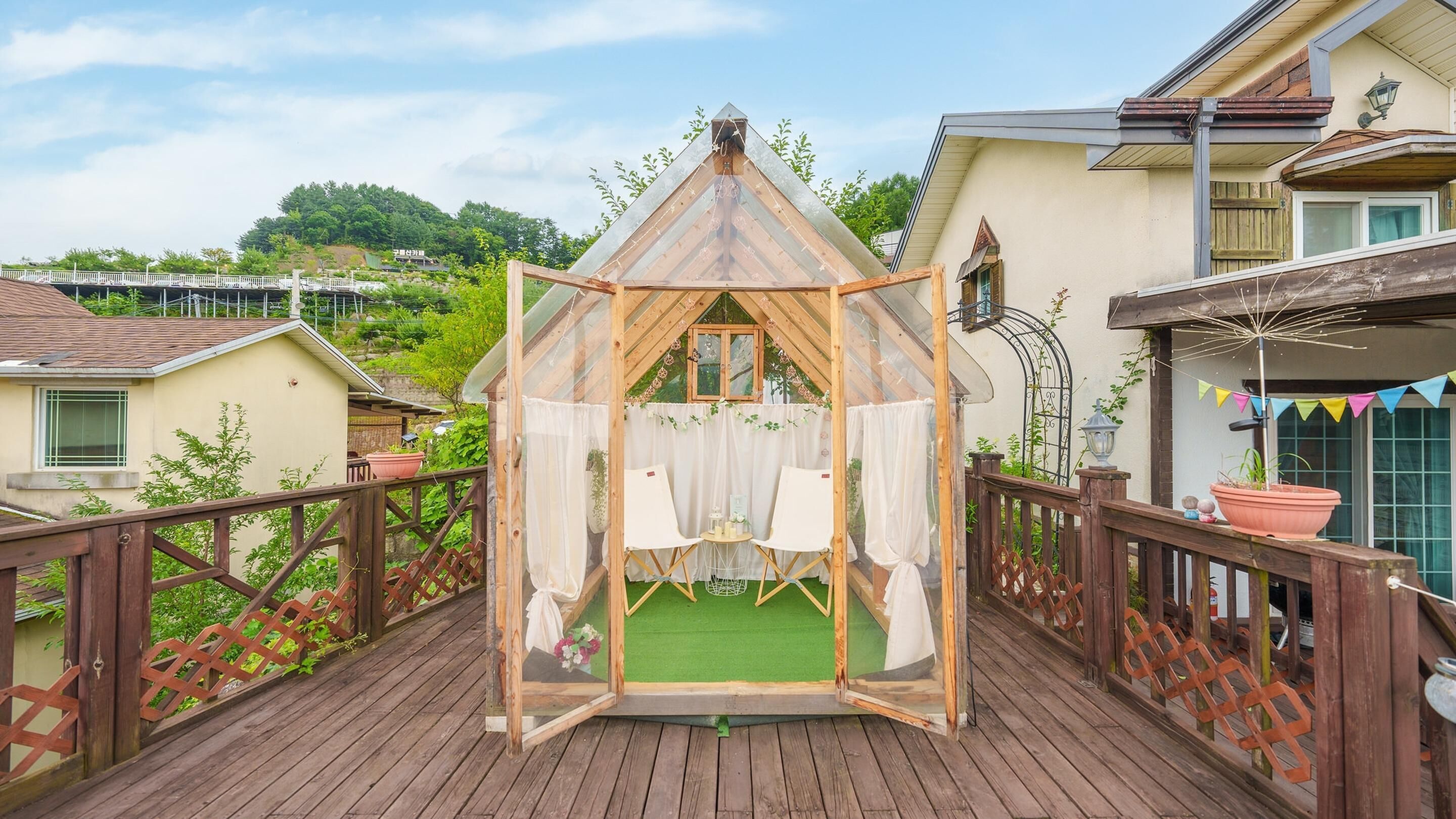 A wooden deck with a gazebo structure, featuring two white chairs and a small table.