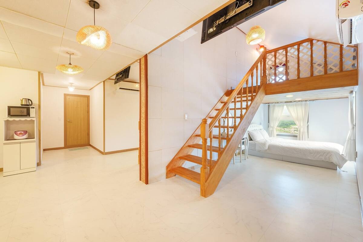 A spacious room with a wooden staircase, a bed, and a kitchen area with a microwave and kettle.