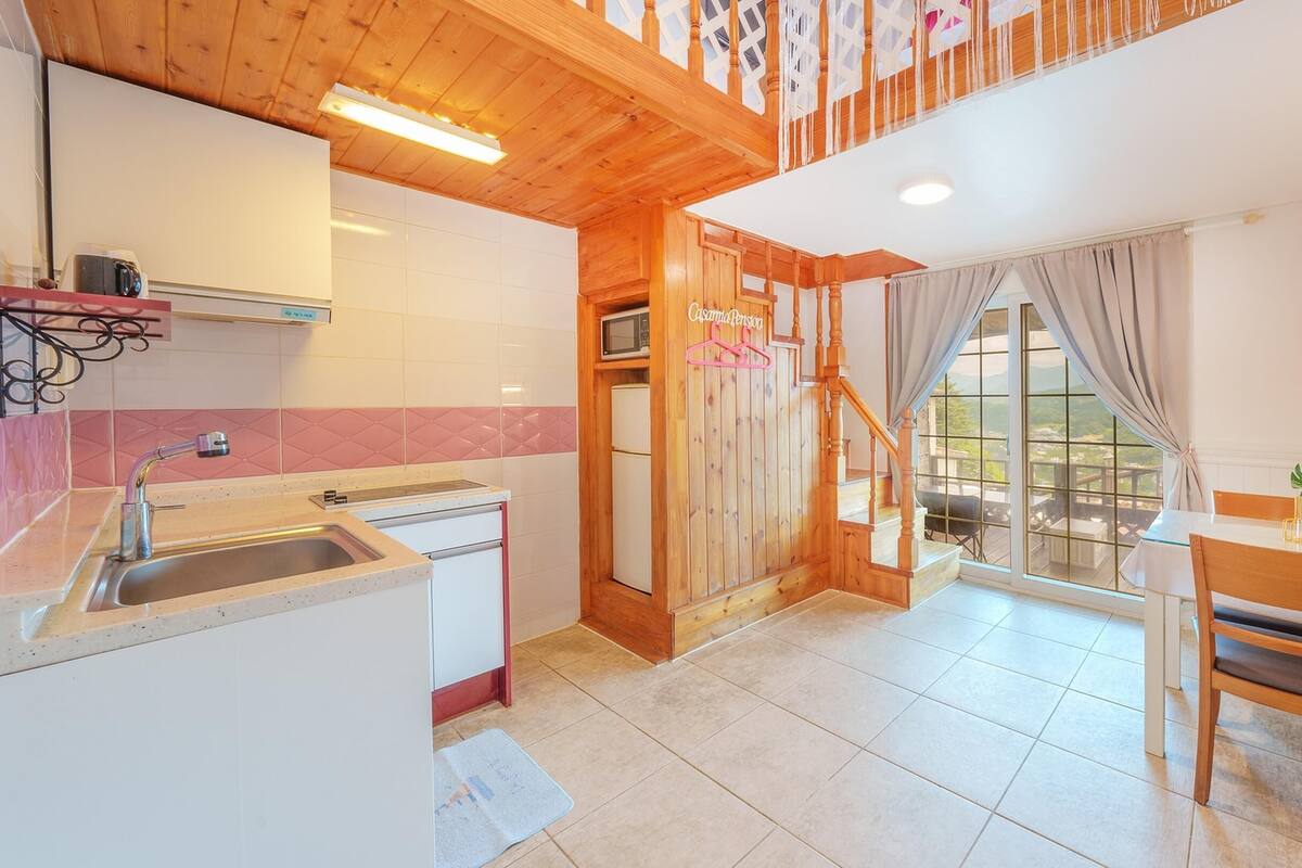 A modern kitchen with a wooden staircase, a dining area with a table and chairs, and a large window with curtains.