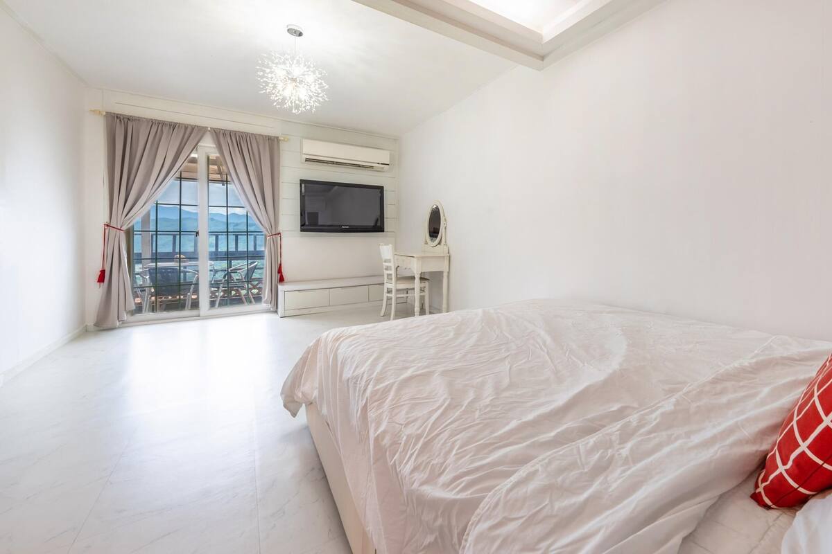 A modern bedroom with a large bed, a TV, and a desk with a chair.