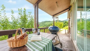 A wooden deck with a table set for a meal, a grill, and a view of a mountainous landscape.