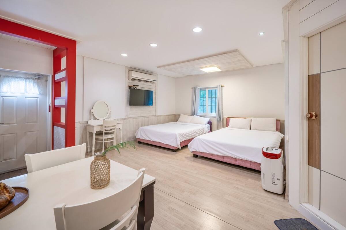 A hotel room with two beds, a dining table with a vase, a mirror, and a TV on the wall.