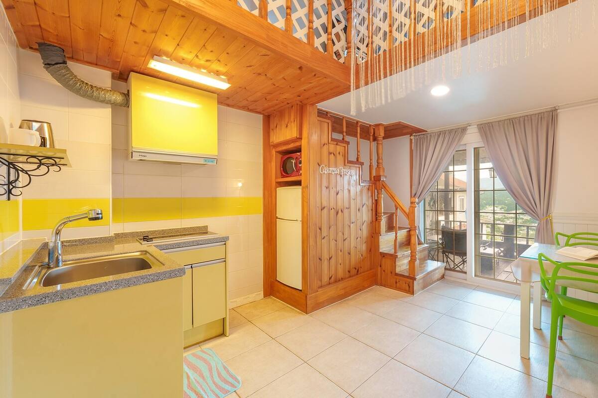 A kitchen with a sink, stove, and wooden staircase leading to a balcony with outdoor seating.