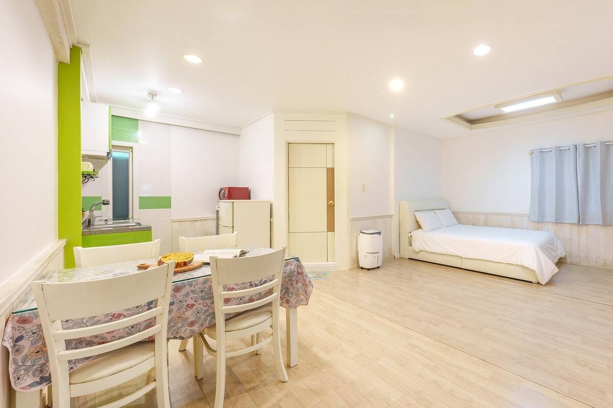 A compact room with a bed, a small table with chairs, a kitchenette, and a window with curtains.