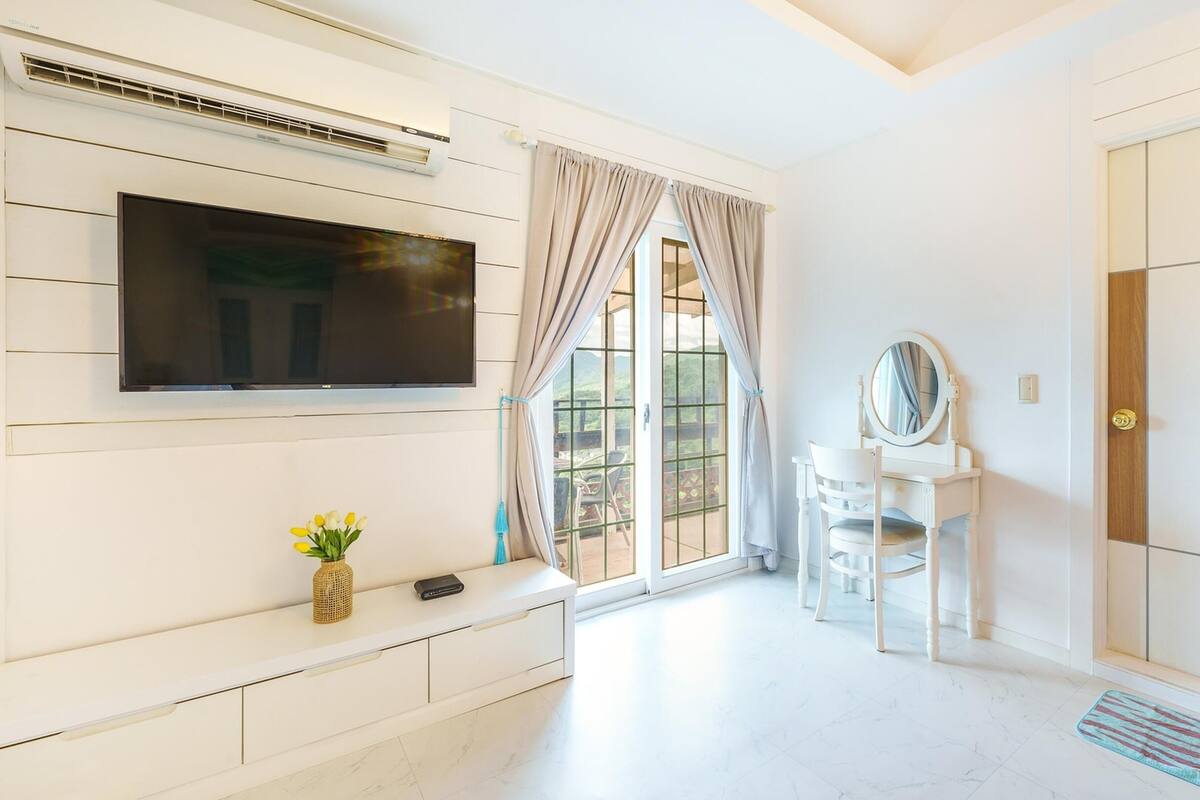 A modern bedroom with a TV mounted on the wall, a vanity with a mirror, and a window with curtains.
