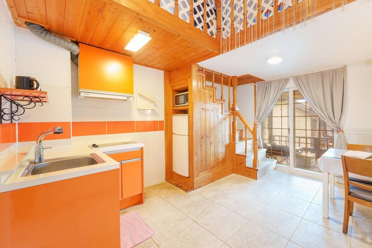 A kitchen with orange cabinets, a sink, and a stove. There is a staircase leading to a balcony with a view.