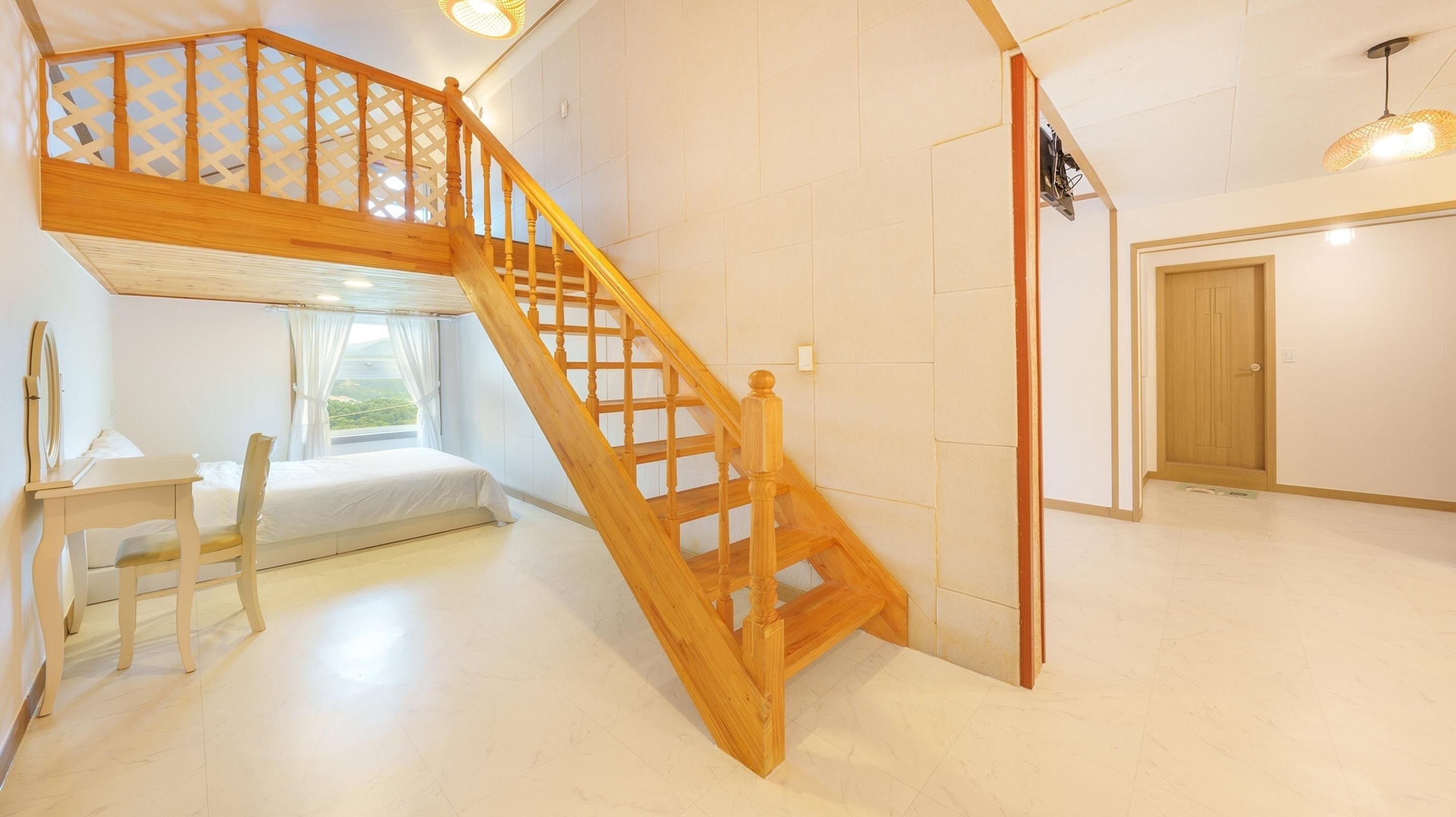 A room with a wooden staircase, a bed, a desk, and a window with a view.