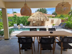 An outdoor pool area with lounge chairs, a wooden table, and a thatched umbrella.