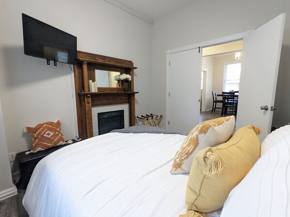 Un dormitorio con cama, chimenea, televisor montado en la pared y puerta que da a un comedor.