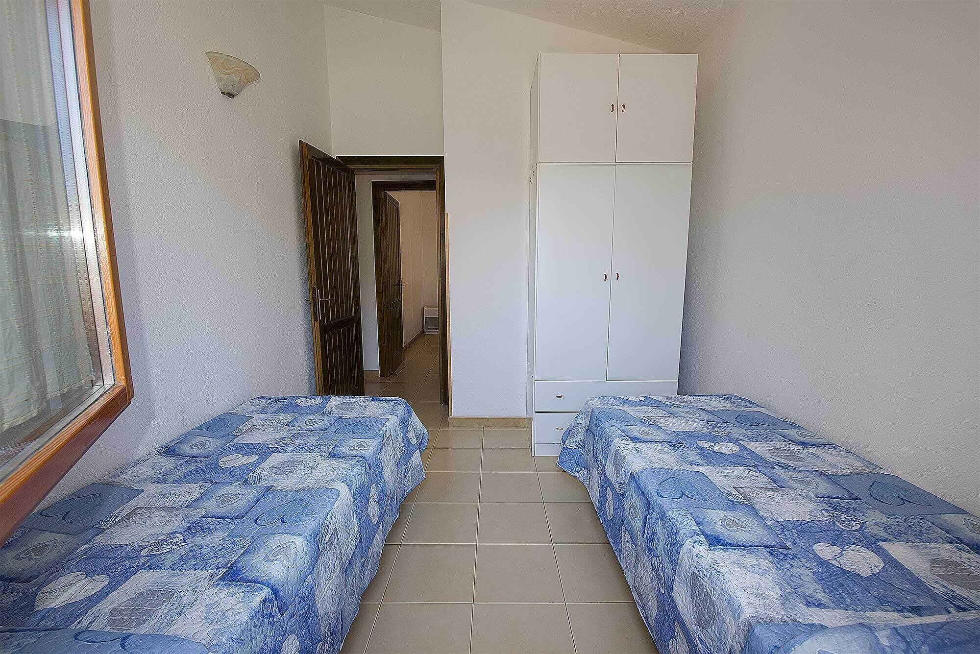 A small room with two single beds, a white wardrobe, and a door leading to another room.