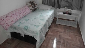 A small, neatly arranged bedroom with a single bed, a bedside table with a lamp, and a window with curtains. - Pousada CNU (Rio de Janeiro)