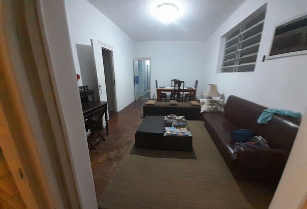 A living room with a sofa, a coffee table, a dining table with chairs, and a door leading to another room.