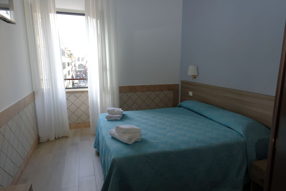 A hotel room with a bed, a view through a window, and a bathroom with a tiled floor.