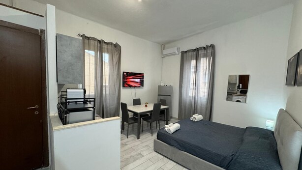 A compact hotel room with a bed, a desk, a chair, a TV, and a small kitchenette. - Civic 10 II Spacious studio apartment with terrace above at Sassari Center (Sassari)