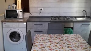 A compact kitchen with a washing machine, microwave, and a table with a floral tablecloth. - Civic 10 II Spacious studio apartment with terrace above at Sassari Center (Sassari)
