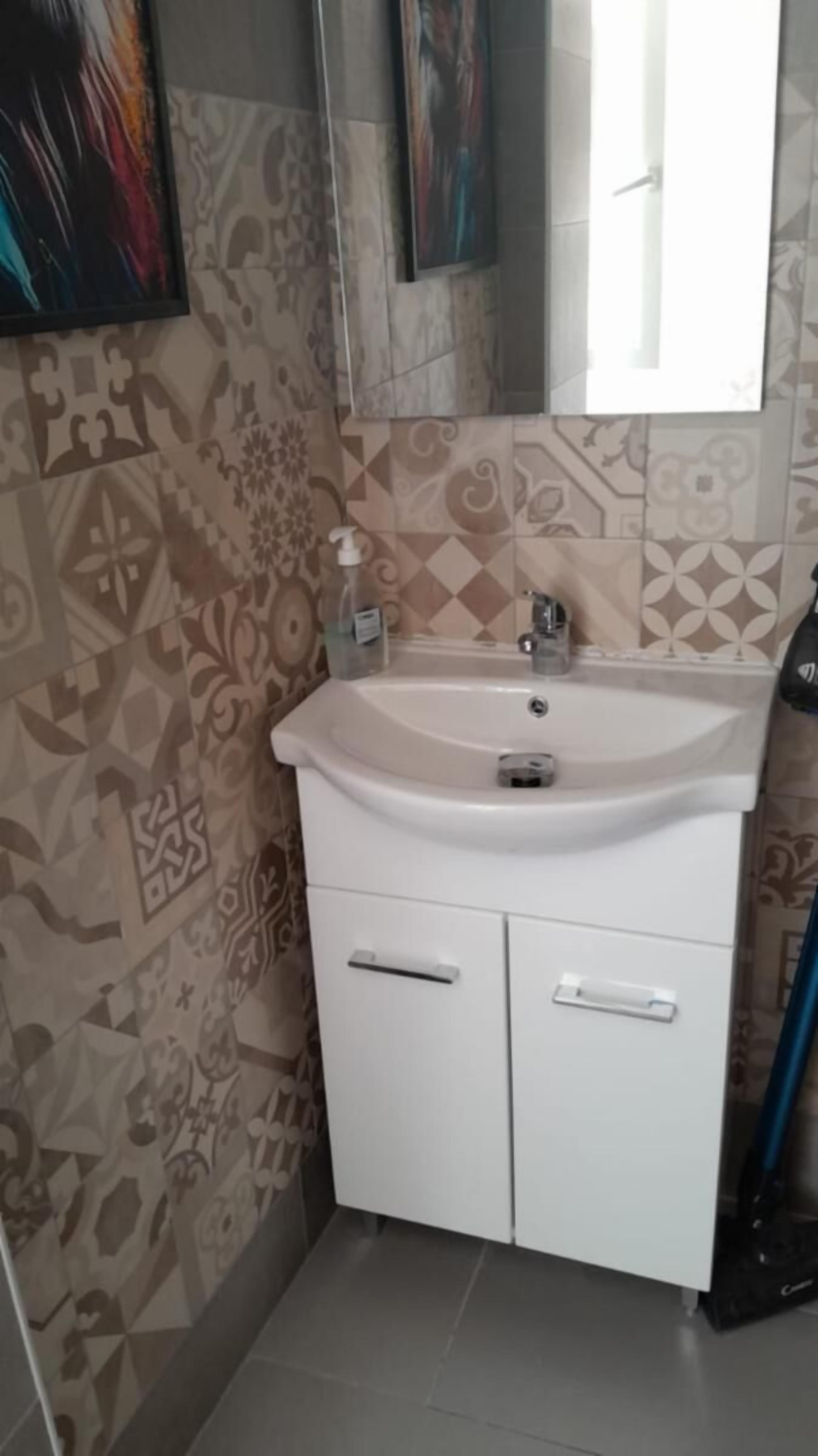 A bathroom with patterned tiles, a white sink, and a mirror above it.