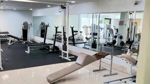 Een sportschool met diverse fitnessapparaten, een bank en een spiegelwand.
