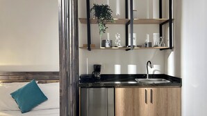 Een moderne keuken met een zwart aanrecht, roestvrijstalen apparatuur en houten kastjes. Er staat een koffiezetapparaat op het aanrecht en een hangplant op de plank.