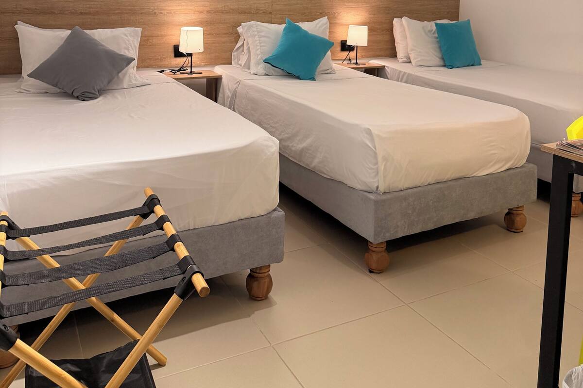Habitación de hotel con dos camas, cabeceros de madera, lámparas de noche y una mesita con lámpara.