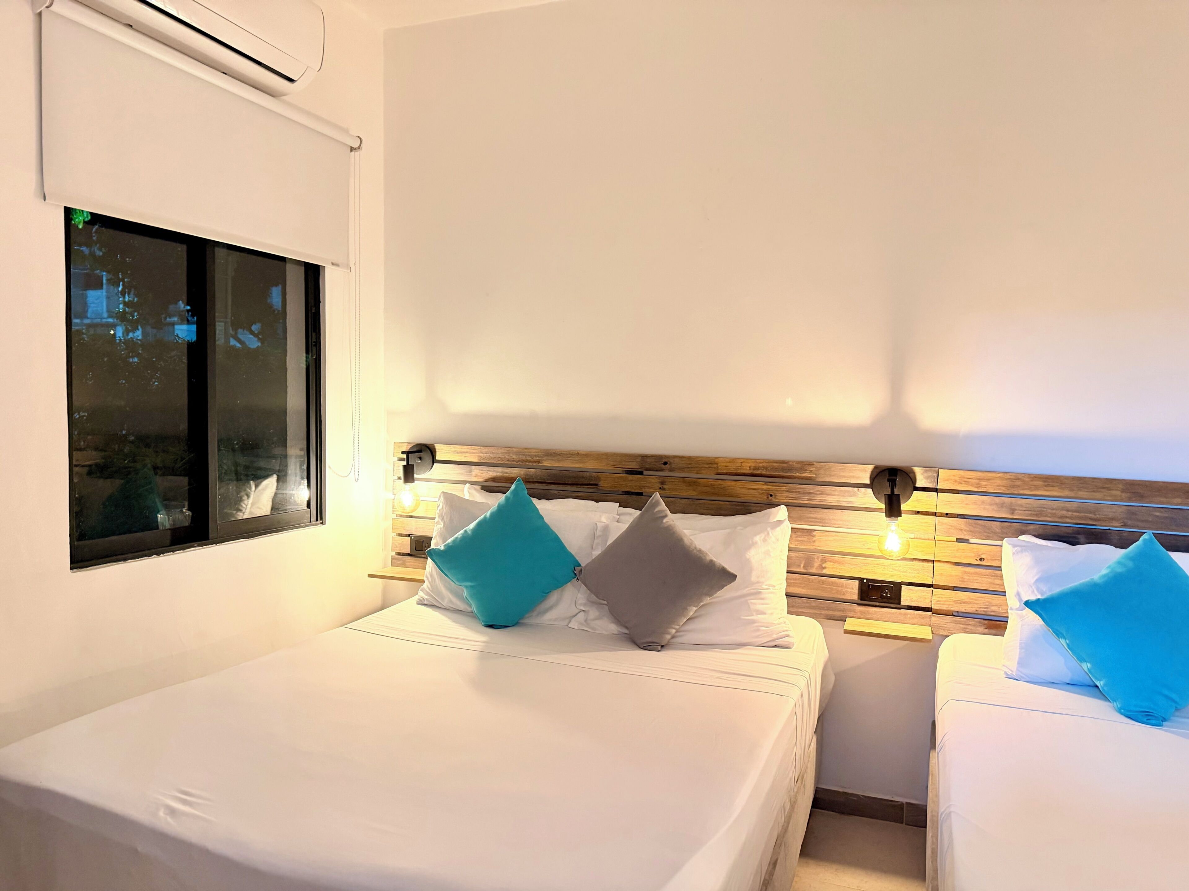 Une chambre d’hôtel avec deux lits, une fenêtre et un luminaire fixé au mur.