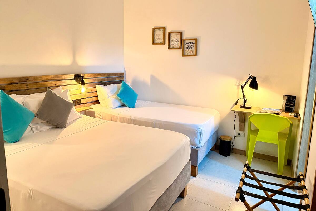 Habitación de hotel con dos camas, un escritorio con lámpara, una silla y un cesto de basura.