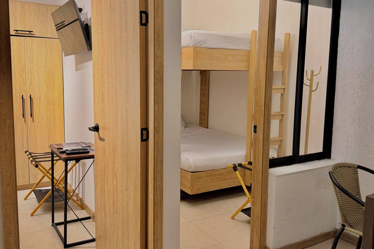Una habitación compacta con una litera, un escritorio con silla, una mesita y un armario.