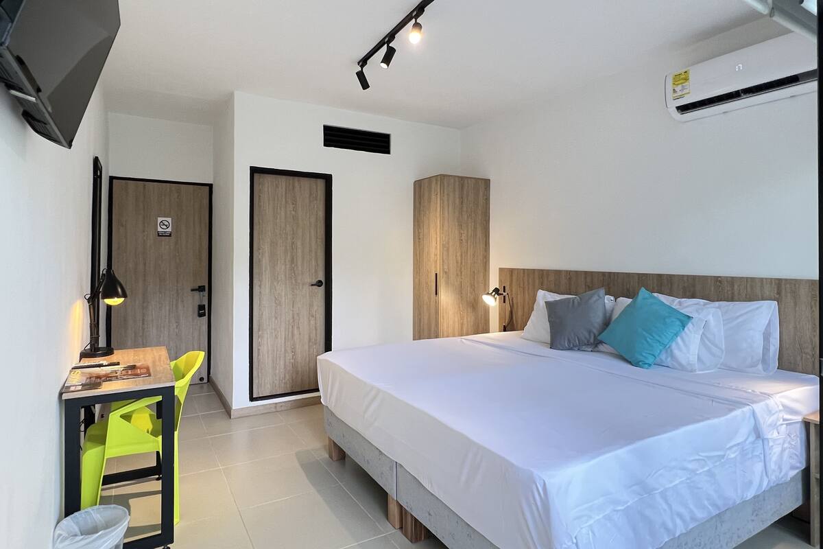 Habitación de hotel moderna con cama, escritorio, silla y televisor montado en la pared.