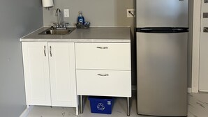 Une cuisine avec des meubles blancs, un réfrigérateur en acier inoxydable, un four à micro-ondes, un évier et une poubelle de recyclage bleue.