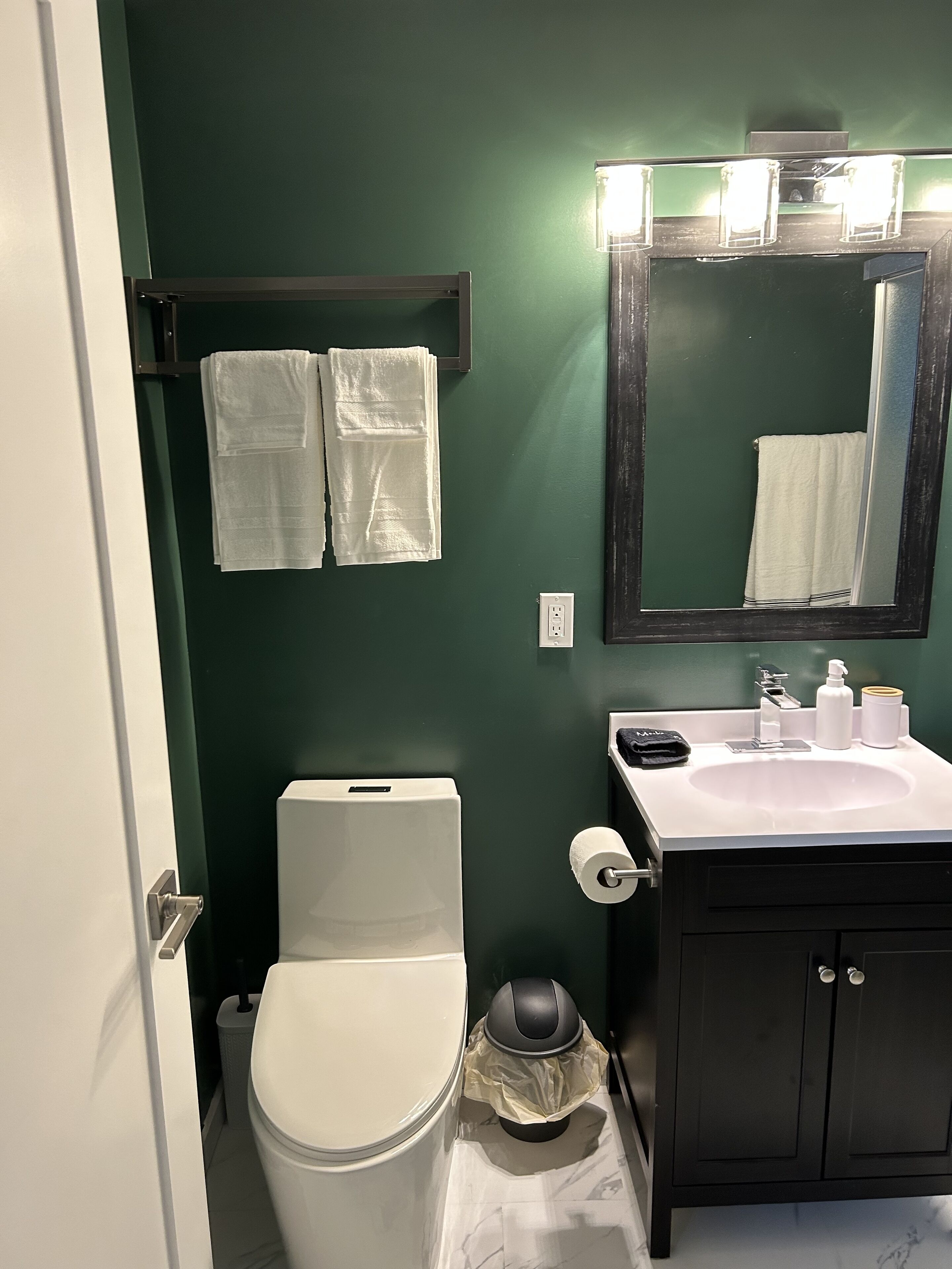 A bathroom with a toilet, sink, and mirror. There are two towels hanging on a rack.