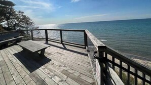 A wooden deck with a railing overlooking a body of water. - Coastal theme/wooded & large deck/fenced-in yard (Holland)