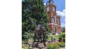 Une église en briques surmontée d’un clocher, entourée d’un jardin où poussent diverses plantes et fleurs.