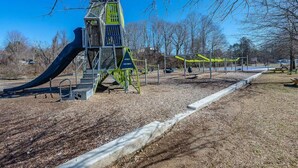 Une aire de jeux avec un toboggan et des structures d’escalade, entourée d’arbres et sous un ciel dégagé.