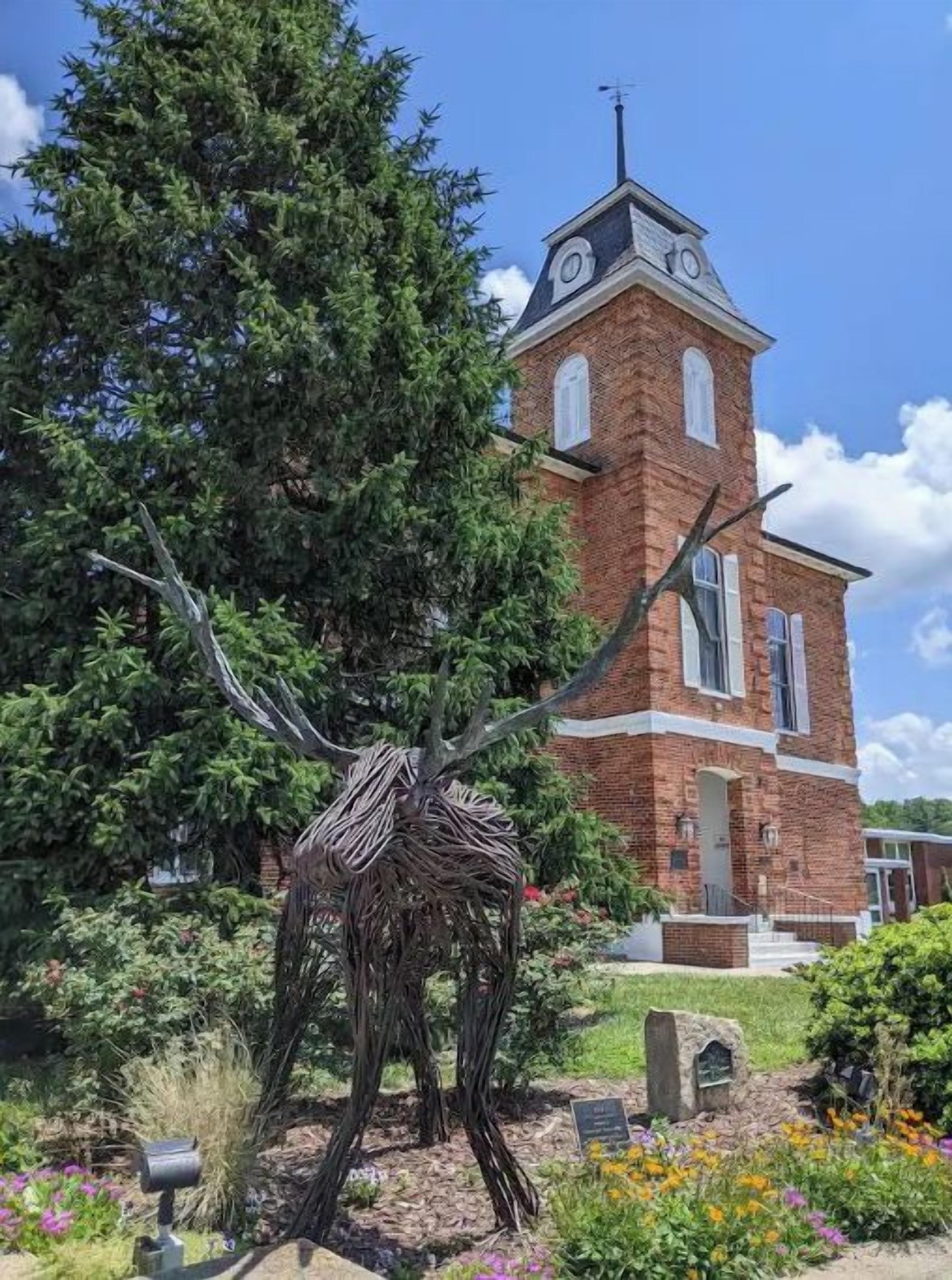A brick church with a clock tower, surrounded by a garden with various plants and flowers.