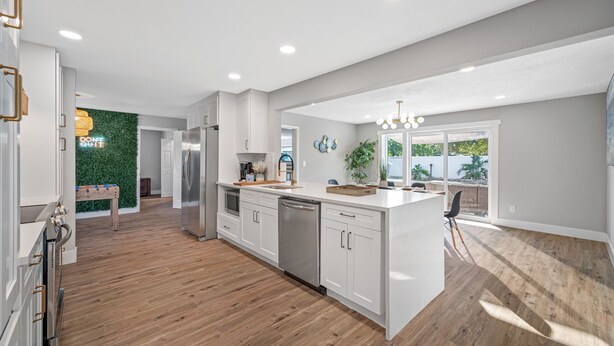 A modern kitchen with white cabinets, stainless steel appliances, and a wooden floor.