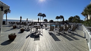 A wooden deck with outdoor seating, a pool, and palm trees. - Grand Pavilion 15 - Oceanfront Home! GP Pool Pass! (Isle of Palms)
