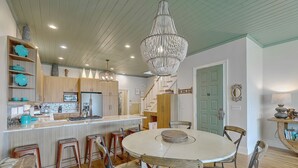 A modern kitchen with a central island, wooden bar stools, and a chandelier. - Grand Pavilion 15 - Oceanfront Home! GP Pool Pass! (Isle of Palms)