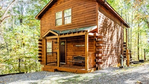 Een houten hut met een veranda, een bankje en een deur waarop 'Serenity Now' staat.
