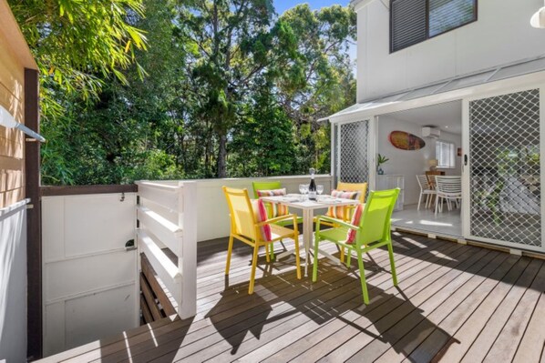 An outdoor patio with a table and chairs, surrounded by a white fence and trees.