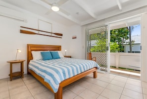 Un dormitorio con cama de madera, mesita de noche, ventilador de techo y vistas al exterior por una puerta corrediza de vidrio.