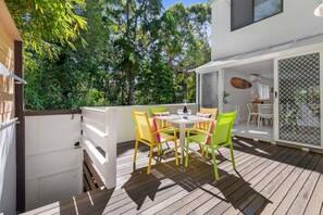 Een terras buiten, met een tafel en stoelen, omgeven door een houten terras en een witte schutting.