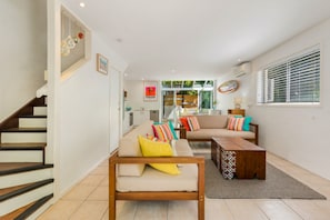 A modern living room with a sofa, coffee table, and a staircase. - Kareela Court 4 Kareela Avenue 14 (Noosa Heads)